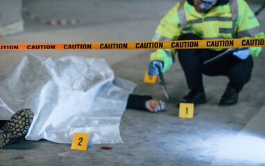 Knife is on the floor. Male detective is collecting evidence in a crime scene near dead body on the construction site