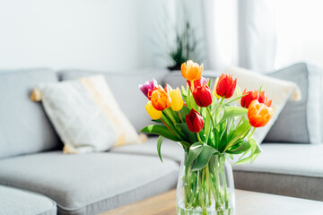 Vase of fresh tulips on the coffee table with blurred background of modern cozy light living room...