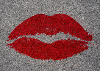 The mark of red lipstick (a pair of female lips), printed on a grey asphalt surface (overhead shot). Grunge imperfections all over it.
