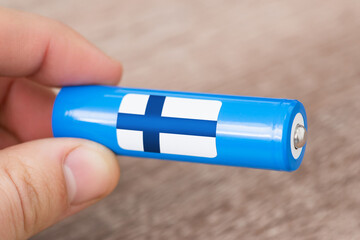 Close up shot of generic li-ion battery in hands of a man with flag of Finland. Producing batteries in Finland, origin of batteries