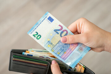 Hands of a girl holding 20 euro bill and wallet full of money, close up. Finances, business in Europe, making purchases concept