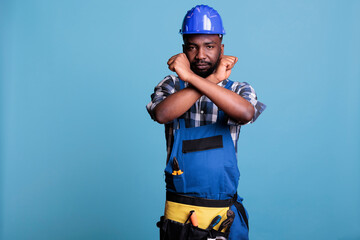 Disapproving african american builder making stop gesture with crossed arms while standing on blue...