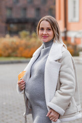 A beautiful young pregnant woman holding her tummy in an autumn park. The expectant mother walks in the fresh air on an autumn day and enjoys the wonderful moments of pregnancy in nature.