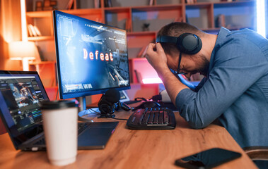 Conception of defeat. Man is playing the shooter game on his computer. Neon lighting