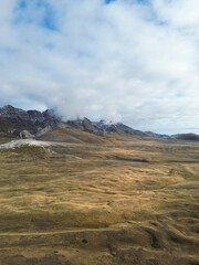 Shot from above of a plain in winter without snow with long roads running through it. Mountains in the background and cloudy sky on a December day.