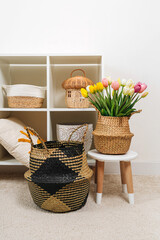 Fototapeta premium Home interior with spring decor. White shelving with various baskets and bouquet of tulips. Seagrass Belly basket , Cloth, and wicker baskets for storage laundry and toys or can use as cachepot.