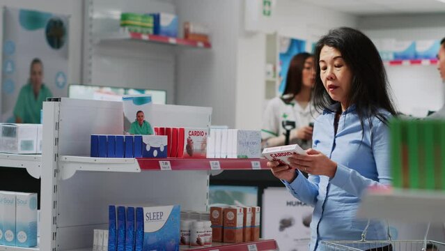 Female customer analyzing pakages of medicine on shelves, looking for disease treatment and supplements. Asian woman reading boxes of pills leaflet to buy healthcare medicaments.