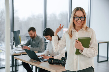 Fototapeta premium Woman in glasses is standing with notepad in hands. Successful team are working together in the office