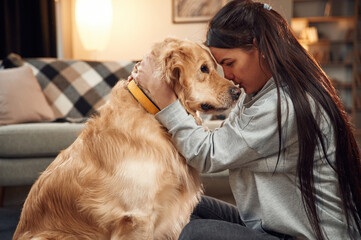 Side view. Having fun, embracing. Woman is with golden retriever dog at home
