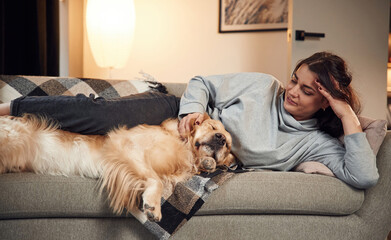 Lying down on the sofa together. Woman is with golden retriever dog at home