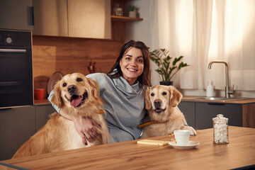 On the kitchen by the table. Woman is with two golden retriever dogs at home