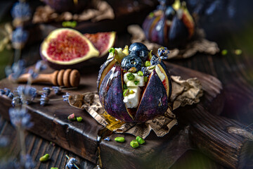 Figs baked with goat cheese, pistachios and honey, decorated with berries and lavender. Vegetarian delicacy. Beautiful still life for a poster. Shot in low key. Image for restaurant interior.