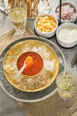 Orange Keta Lachs Kaviar in Dose auf Eis in Glas Schale mit Perlmutt Löffel, Sekt Champagner, gekochte Eier Würfel, Charlotten Zwiebel Würfel, Toast Brot und Saure Sahne auf Serviette und Marmor hell
