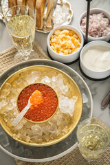 Orange Keta Lachs Kaviar in Dose auf Eis in Glas Schale mit Perlmutt Löffel, Sekt Champagner, gekochte Eier Würfel, Charlotten Zwiebel Würfel, Toast Brot und Saure Sahne auf Serviette und Marmor hell