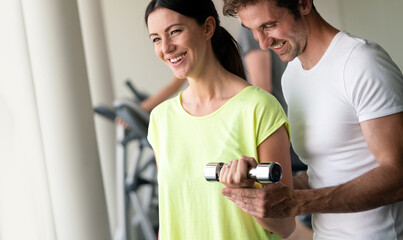 Man trainer flirting with beautiful young woman while helping her at gym