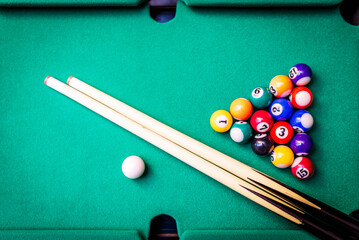 Billiard cues and pyramid of multicolored snooker pool balls on green billiard table.