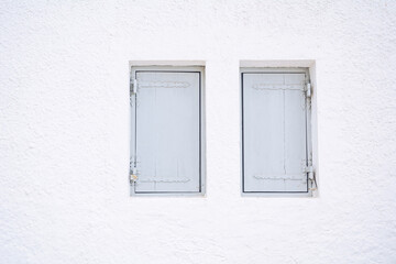 Two closed wooden window shutters painted in light blue gray on a white wall