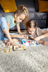 Two little sister girls play with multi-colored toy blocks at home in the living room. Educational games for children. Mess in the game room.