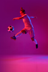 Fototapeta na wymiar Young professional female football, soccer player in motion, training, playing over gradient pink background in neon light. Jump kick