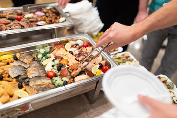 Obraz premium Hand picking up the food by using tongs at self service table on event at hotel or restaurant