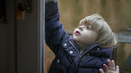 Toddler boy opening front entrance door. Child opens doorknob3