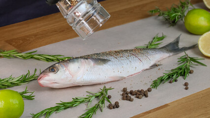 Mullet fish with marinade. Pepper the dish with pepper grinder. Spices and sauce are mixed with fish. Pepper the raw fresh fish for frying. Home kitchen, Culinary master class close-up