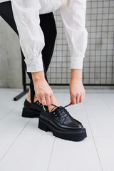 Female legs in trendy black leggings and loafers, laces on leather shoes, details of a stylish autumn fashion look