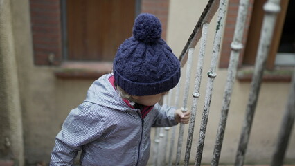 Little baby toddler going up the stairs holding on handrail wearing winter clothes. Child up the...