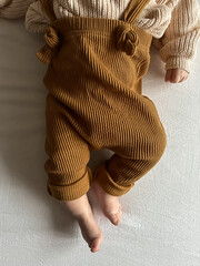 A stylishly dressed baby in a knitted sweater and brown pants with suspenders lies on a light background. Scandinavian style in children's fashion