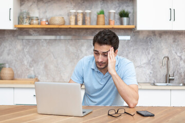 Stressed man working on laptop in the kitchen at home. Distance work concept	