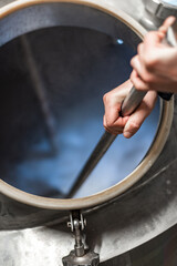 A man stirs mash in a stainless steel kettle at a craft beer brewery