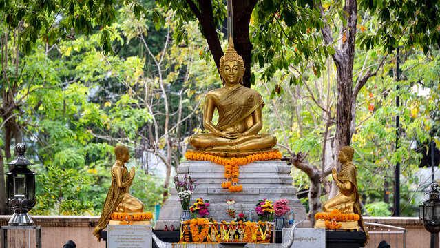 A golden statue of a seated Buddha surrounded by his disciples (a small temple in a park in Bangkok)