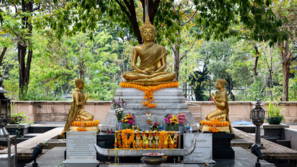A golden statue of a seated Buddha surrounded by his disciples (a small temple in a park in Bangkok)	