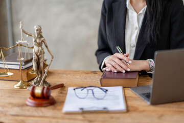 Professional Asian female lawyer or legal advisor sitting at her desk holding hands on books on...