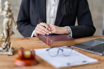 Professional Asian female lawyer or legal advisor sitting at her desk holding hands on books on...