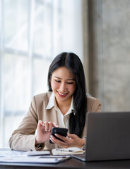 Asian businesswoman holding and dialing the phone to contact customers with financial details Earnings and benefits in the office with a happy smile.