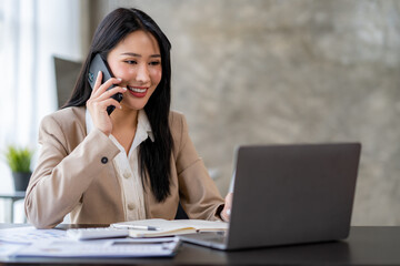 Asian businesswoman sitting on the phone with a customer explaining financial details Earnings and benefits in the office with a happy smile.