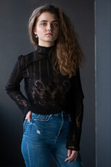 Beauty portrait of a pretty young woman, dressed in a black suitcase and jeans, over grey background.