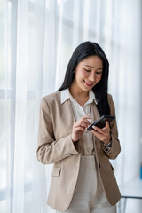 Obraz premium A beautiful Asian businesswoman stands and presses the phone to make customer contact explaining online marketing strategy, and finances in the office happily.