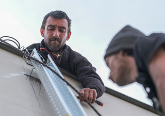 team of electrical engineers installing chutes for the supply of electricity from a solar panel installation using a wireless drill