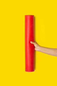 Mano de mujer sosteniendo una esterilla de yoga roja sobre un fondo amarillo brillante liso y aislado. Vista de frente y de cerca. Copy space. Formato vertical