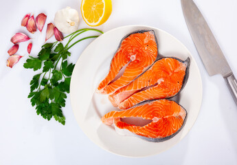 Uncooked salmon steaks on plate with parsley and lemon. Seafood on table, isolated over white background.