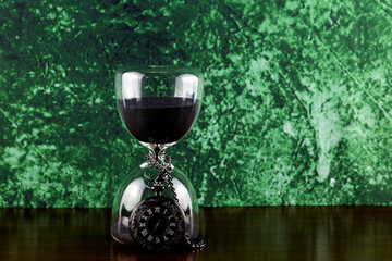 Black Pocket Watch with Hourglass on a Wooden Surface