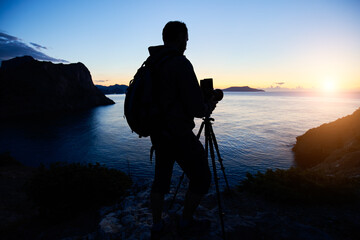 Silhouette of photographer on top of mountain at sunset background. Nature photographer in the...