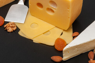 Different types of cheese on a wooden board decorated with grapes, dried apricots and nuts
