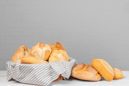 Fresh italian wheat breads in the basket on the table on white wall background. Homemade baked various loaves of wheat, assorted grain breads and bun. Bread background, copy space