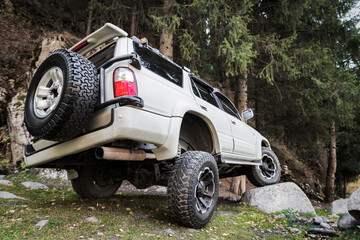 White off-road car in travel on mountain forest, Tuned reinforced suspension helps to overcome obstacles. © Roman