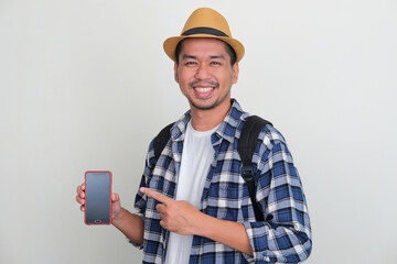 Asian backpacker smiling at the camera while pointing to blank phone screen that he hold