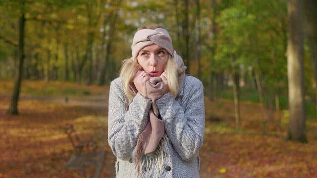 Front view of young, blonde woman walking in park in cold weather. Beautiful woman wearing stylish clothes, standing, warming, looking at camera. Concept of autumn and fall.