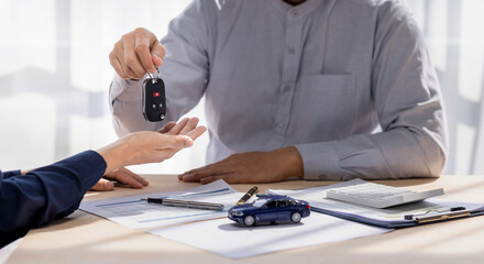 Dealer salesman giving car key to owner. client signing insurance document or rental car lease form...